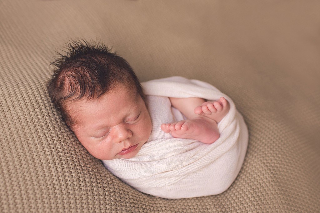 newborn boy wrapped in cream fabric during baby photography session